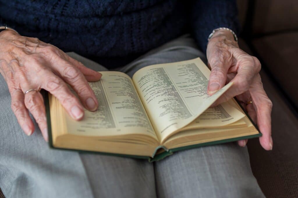 Mains d'une Personne Âgée Lisant un Vieux Dictionnaire Mains ridées d'une personne âgée feuilletant un vieux dictionnaire aux pages jaunies posé sur ses genoux.